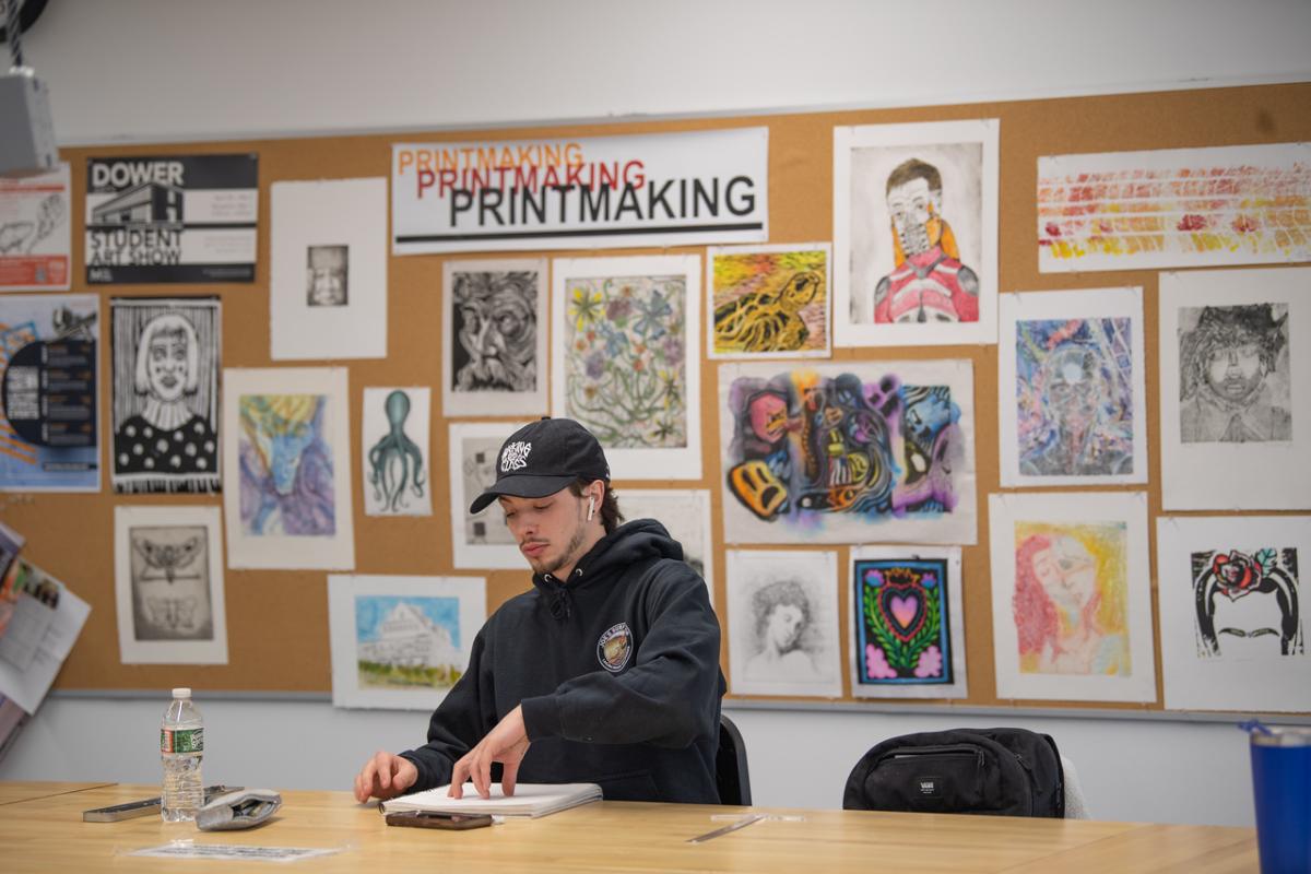 Student in an art class with a bulletin board of colorful student prints behind him.
