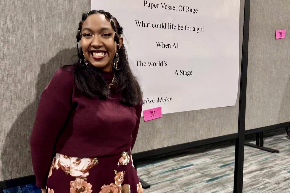 English student smiling in front of written poem.