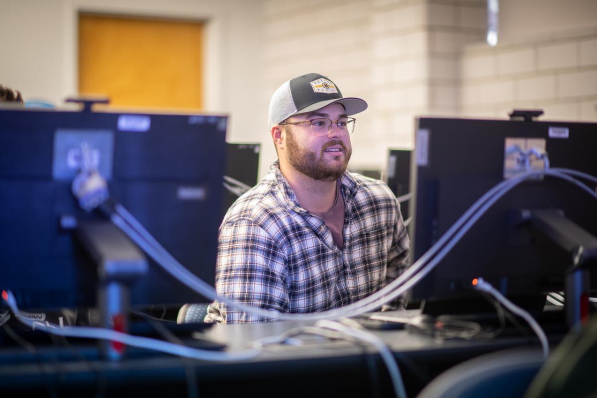 Management student smiling in a classroom, seated behind a computer.