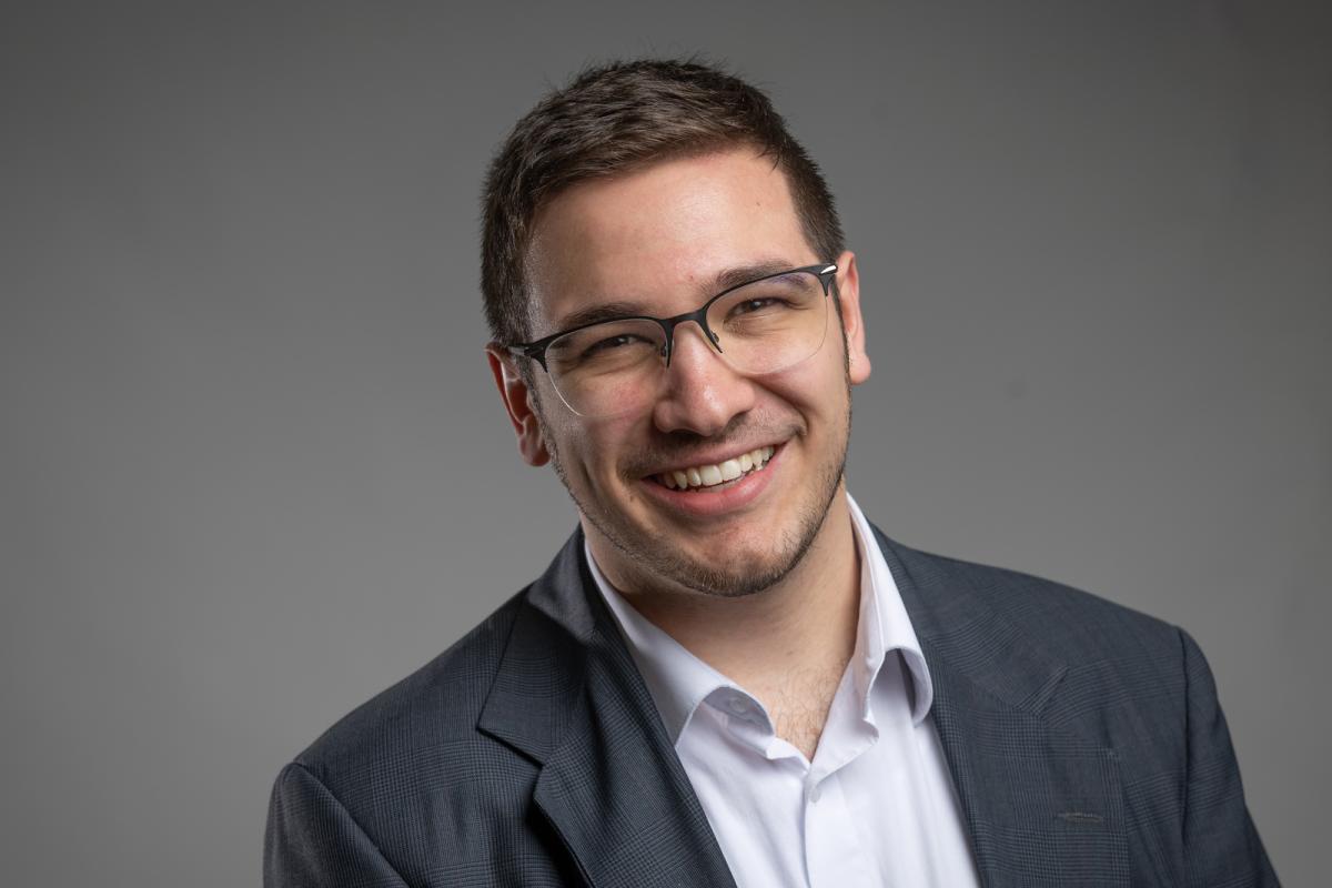 Smiling student intern in a suit jacket against a plain gray background.