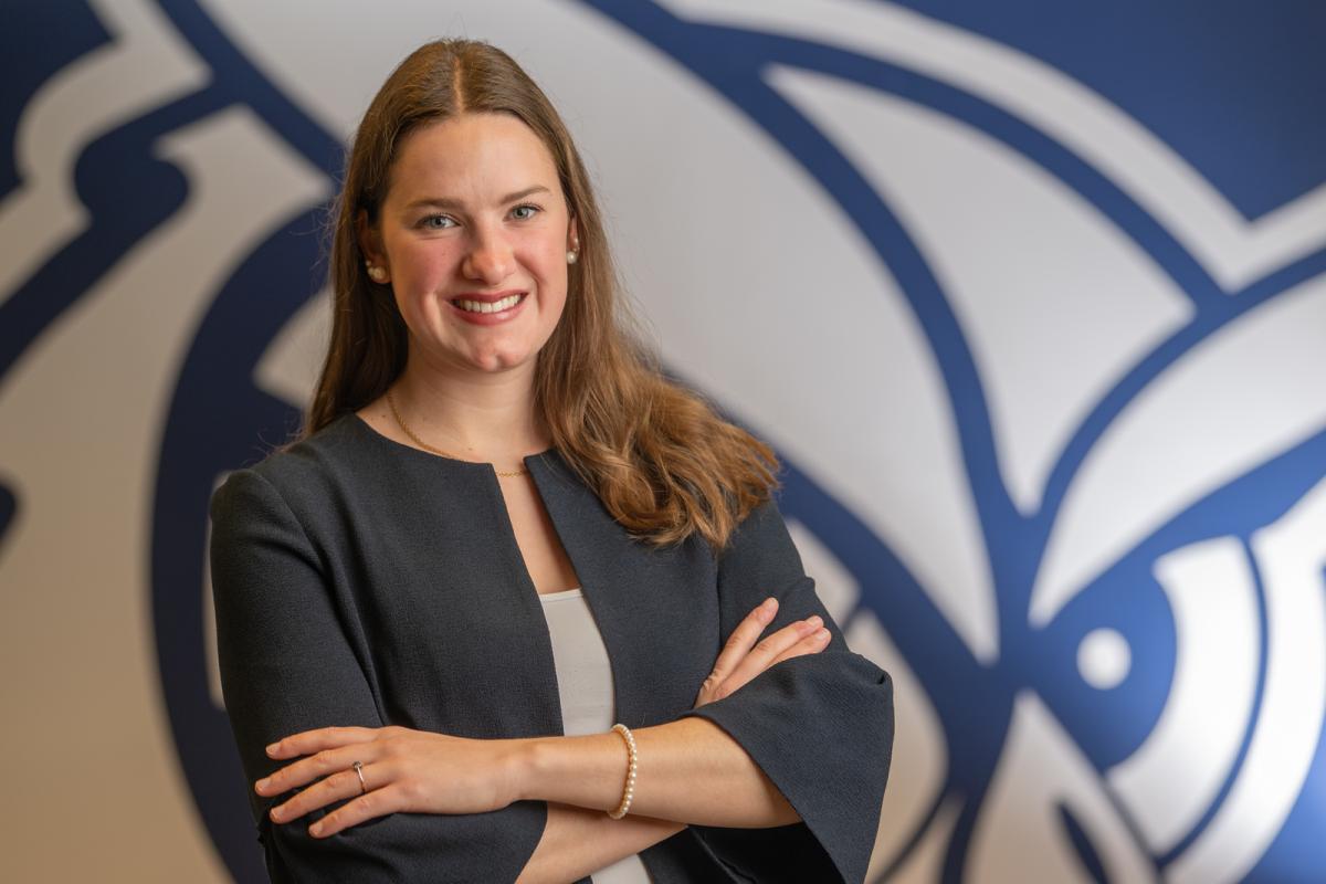Student smiling confidently with arms crossed, standing in front of the WSU owl logo.