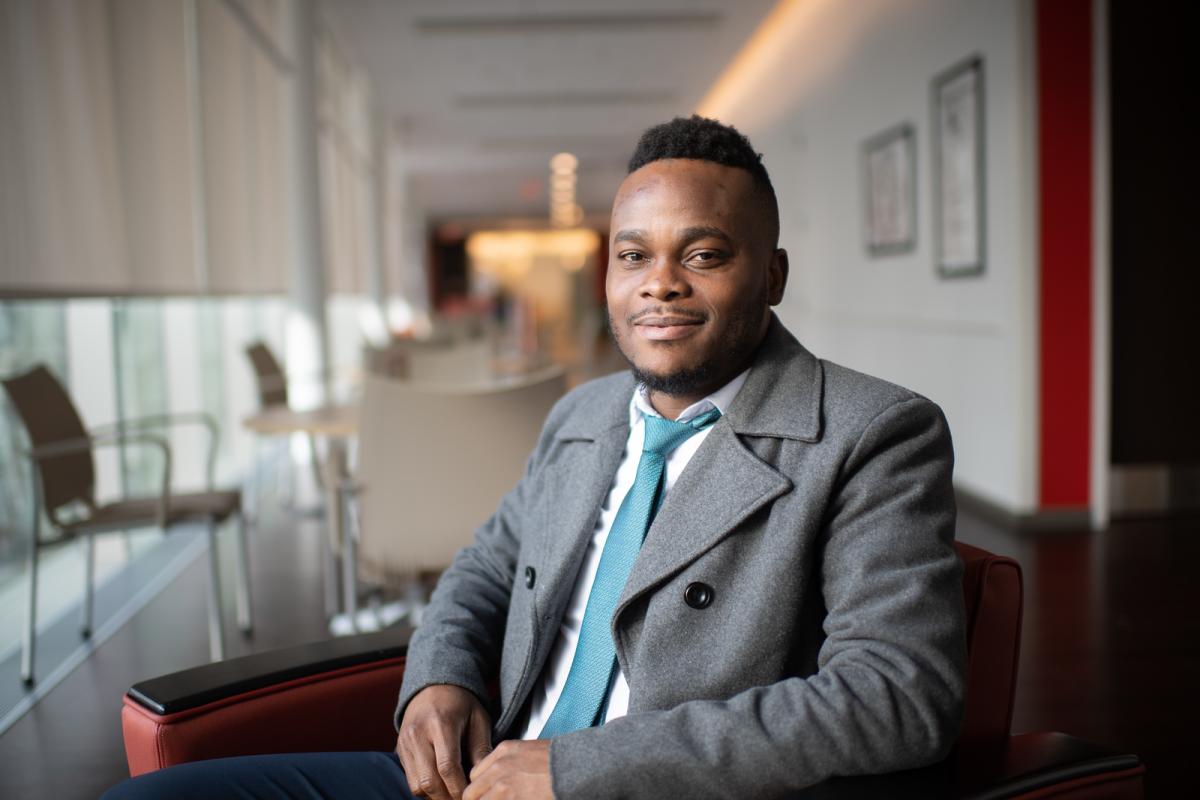 MPA student in a coat and tie smiling inside a campus building.