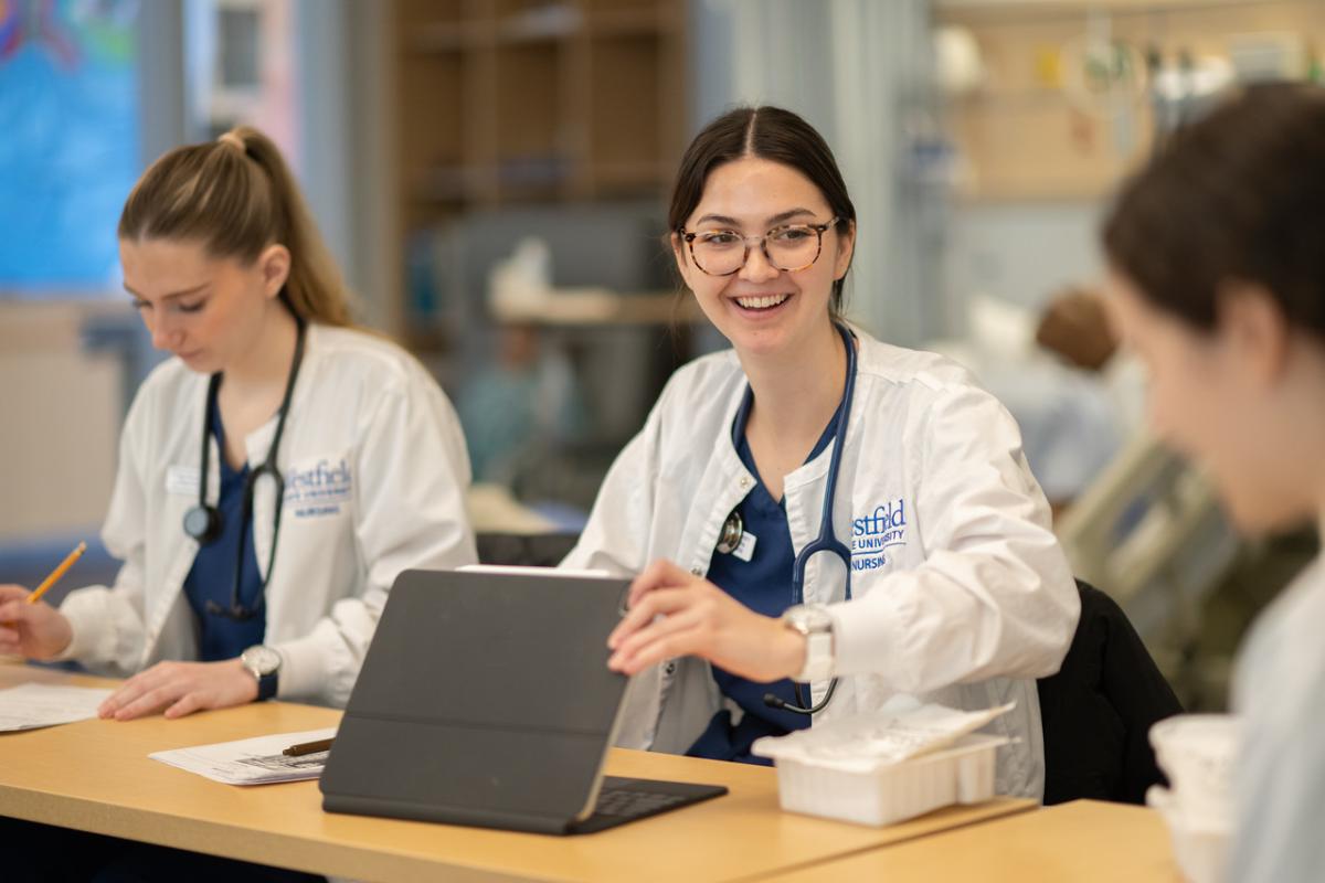 Smiling nursing student opening a laptop in a classroom.