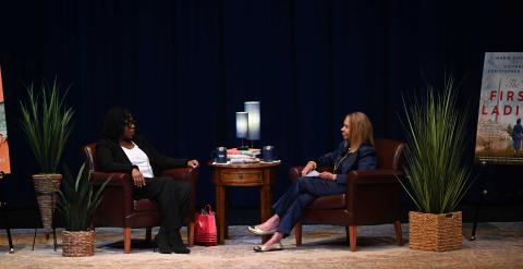 two women sit on a stage in conversation