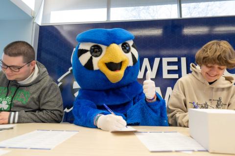 Blue owl mascot shows a thumbs up while two students write notecards
