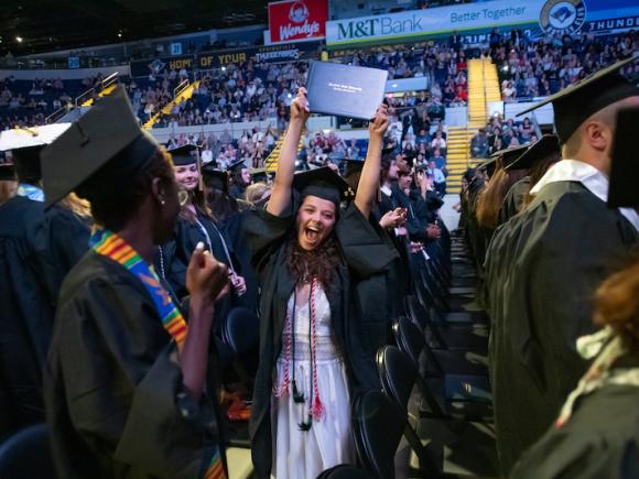 Students cheer and raise their diplomas at commencement.