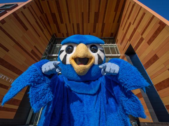 Nestor the Owl, pointing toward the camera, under the University Hall awning