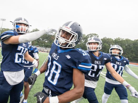 WSU football ream wearing blue jerseys with "Owls" written on them. Group of four students at game in uniforms.