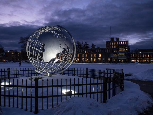 Campus globe at night lit up with snow surrounding it and dark clouds in the sky.