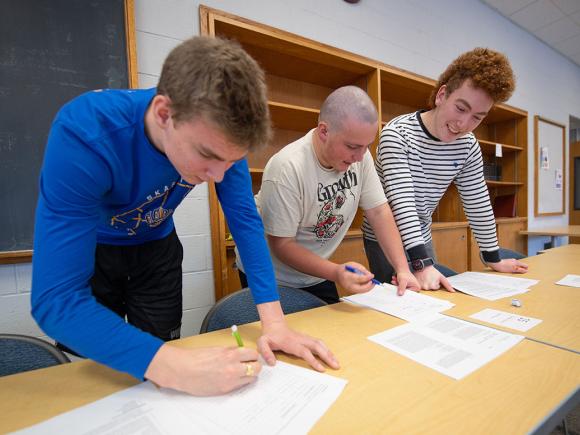 Three students work together on coursework in a history classroom.