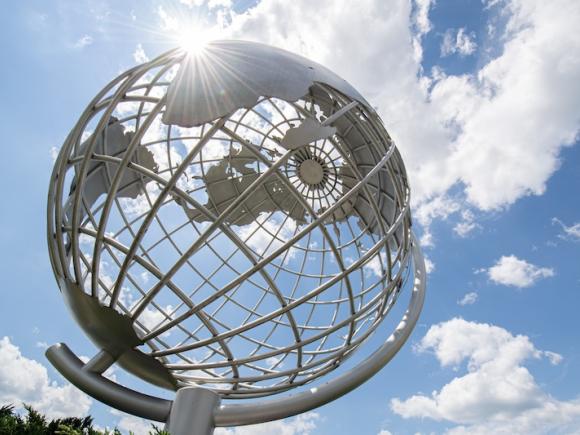 A stock photo of the campus globe. The sun shines above and there are clouds in the sky.