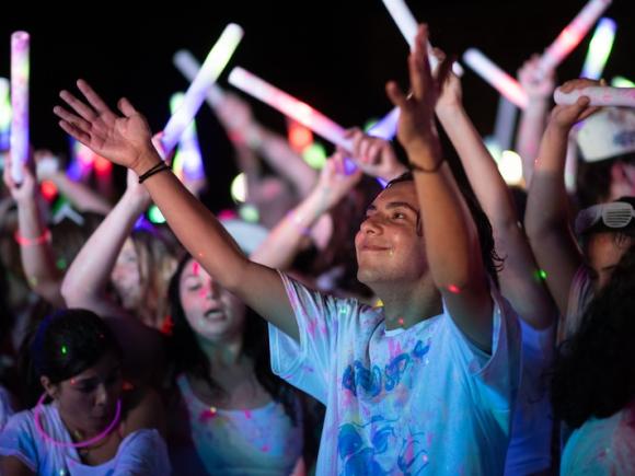 A student has his hands out during this year's Glow Party with people dancing behind him, also holding glow sticks.