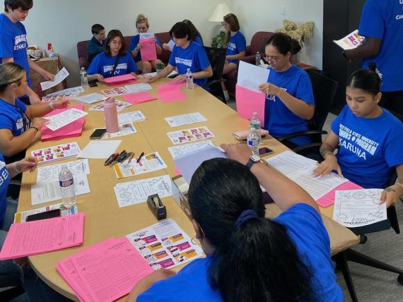 Several new Honors students working together at a table covered in papers for their two-day orientation to the campus. 