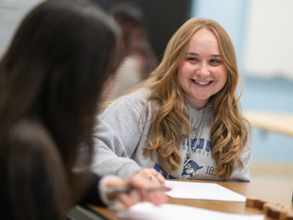 Student math tutor smiling helping another student with homework.
