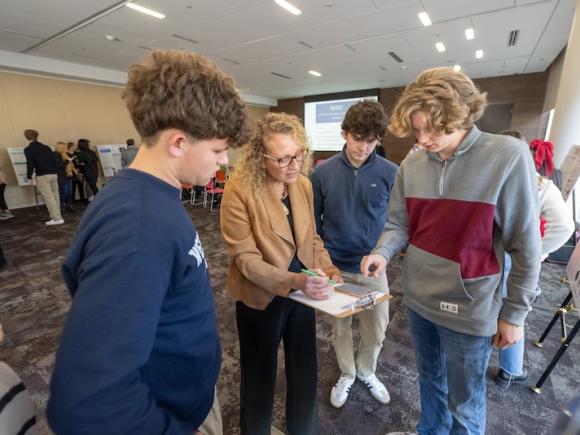 Three young men presenting a poster board and their idea to Dr. Vanessa Diana as part of Discover Westfield's Shark Tank event.