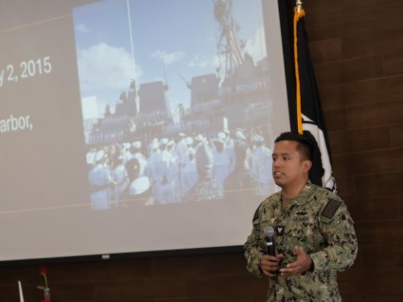Josue “Alex” Ramos, Navy veteran and former Veterans Affairs work-study student at Holyoke Community College, speaking at Veterans Day at Westfield State. A projector behind him is showing a photo from Pearl Harbor, 2015.