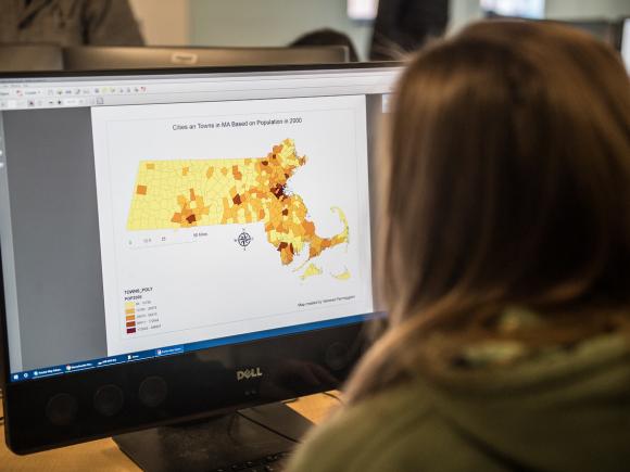 Student in a GIS mapping class working at a computer, viewing a population-based map of cities and towns.