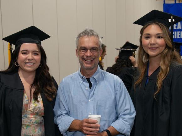 Faculty member smiling with two students at commencement ceremony.