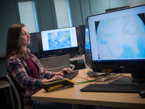Urban and Regional Planning student seated at a computer with maps of the Earth.