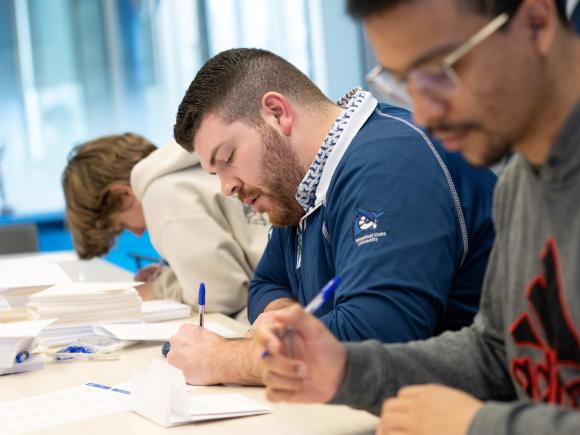 Three people sit at table and write on notecards