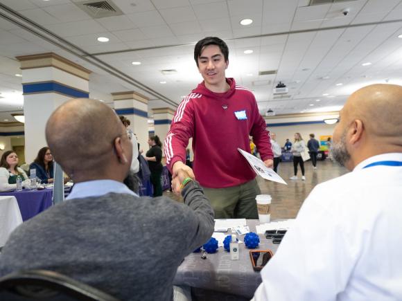 Student shaking hands with an employer at a career fair event.