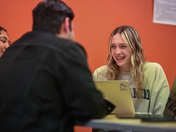 Student with a laptop laughing while chatting with fellow students.