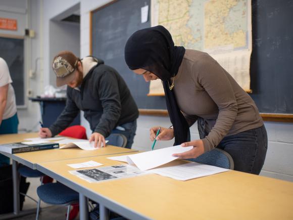 Students working on a project in a history class with a map displayed behind them.