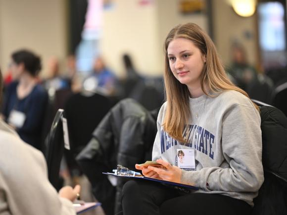 Student listening and taking notes during an on-campus event.