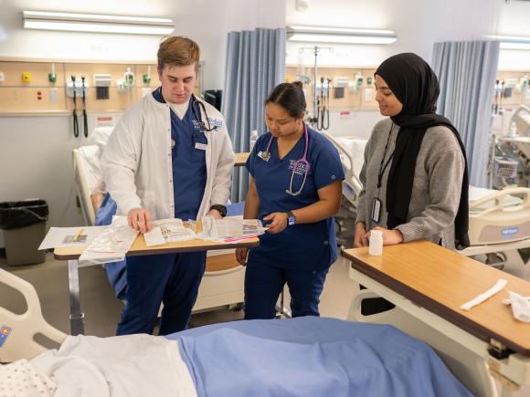 Three nursing students collaborating in a simulation lab with medical equipment.