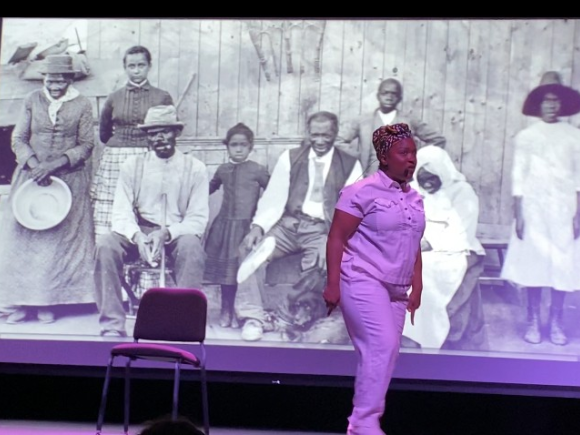 Woman performs on stage in front of black and white image of African Americans in the 19th century