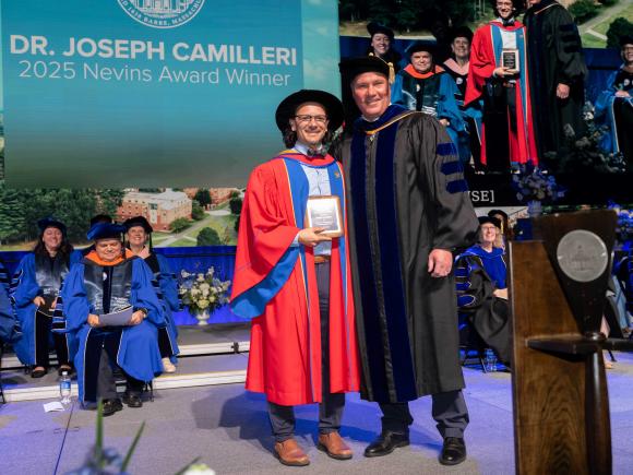 Two men stand on stage in academic regalia