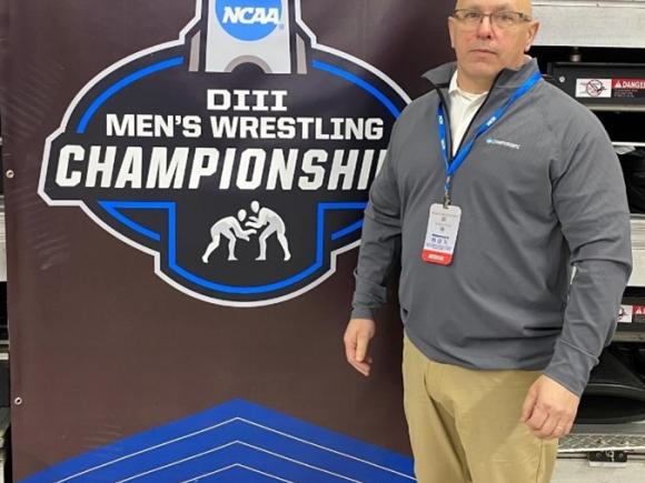 Paul Higgins stands next to banner for NCAA DIII Wrestling Championship