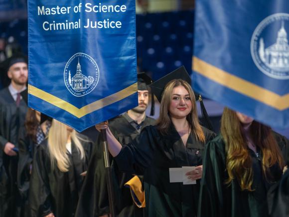 Student holding an M.S. in Criminal Justice flag at commencement.