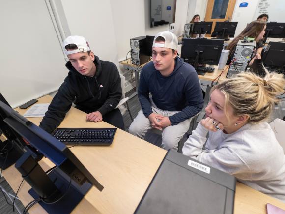 Three students working on a classroom project together at a computer.