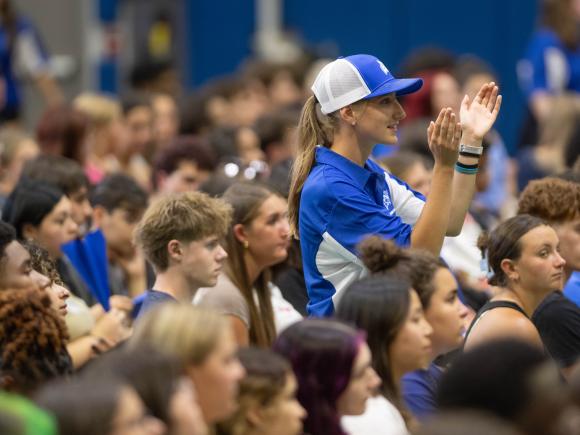 Students sit in audience and listen while one student leader stands and applauds