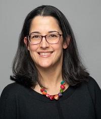 Shakira wearing black shirt, glasses, and a colorful necklace smiling.