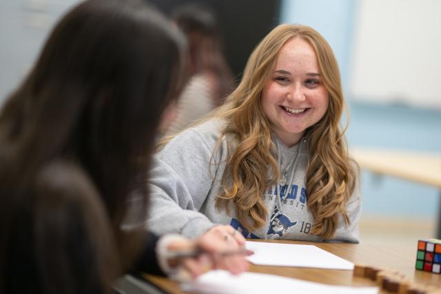 Student math tutor smiling helping another student with homework.