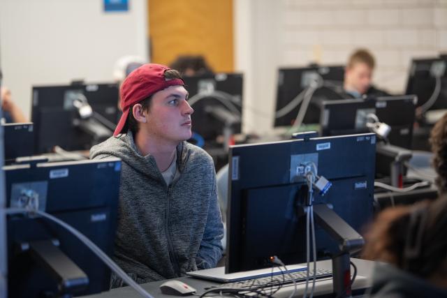 Student in a computer lab wearing a red baseball hat.