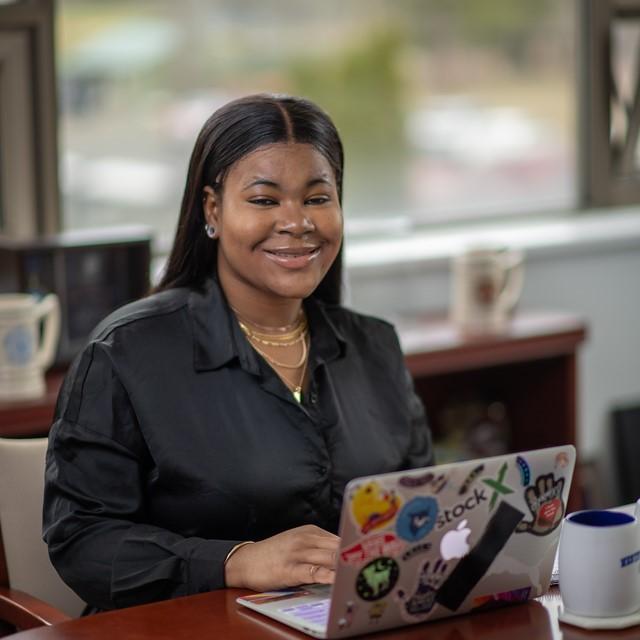 Student at an internship smiling in front of a laptop.