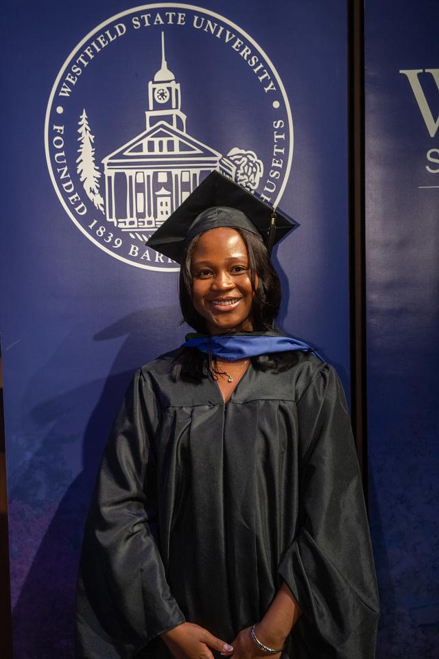 A Physician Assistant student in a cap and gown smiles at commencement.