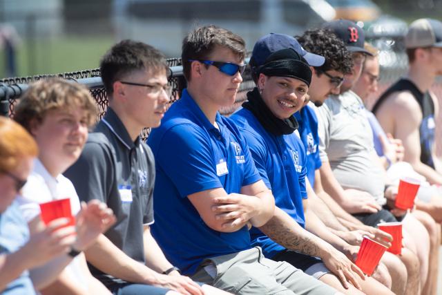Physical education student smiling while seated on bleachers with classmates.