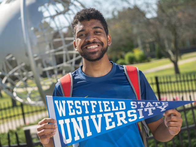 Student at the campus globe smiling holding a Westfield State flag.