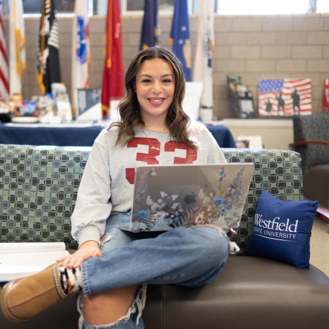 Student smiling working on a laptop in the Military Excellence Center.