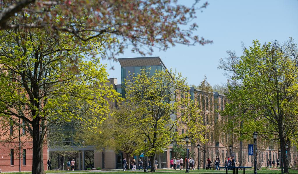 Campus in the spring with trees budding and students walking into campus center.