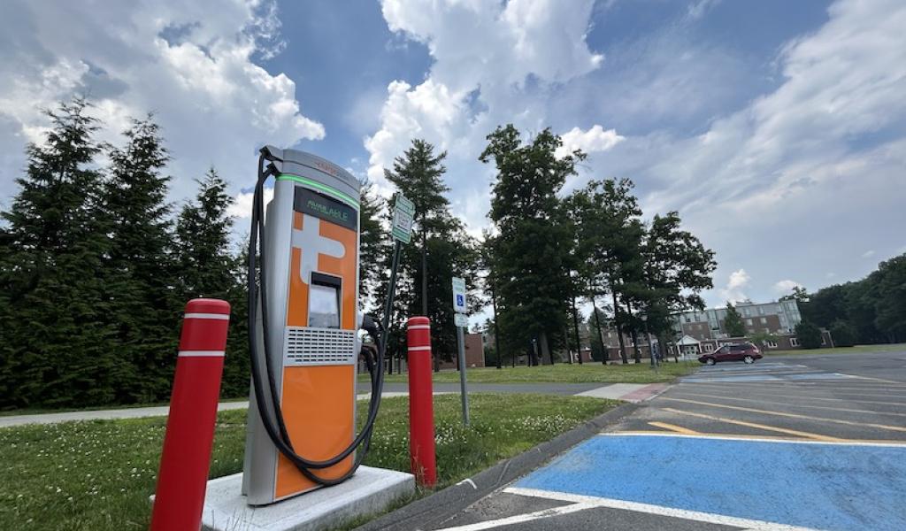 The electric vehicle charger in the Commuter Lot. It is an orange machine and flanked by two, red safety pillars.