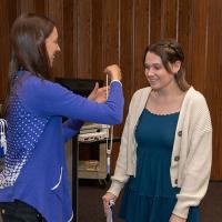 A student smiles as they receive a test tube on a lanyard.