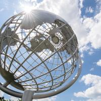 A stock photo of the campus globe. The sun shines above and there are clouds in the sky.