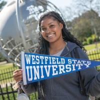 Smiling student holding a Westfield State University flag in front of the campus globe.